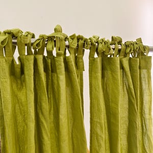 May include: Close-up of green curtains suspended from a silver rail. The curtains, a solid, textured green, are attached to the rail with matching green fabric ties. The curtains are made of a soft, flowing material.