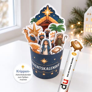 Könnte beinhalten: Ein dunkelblauer, zylindrischer Adventskalender mit einer Krippenszene aus ausgeschnittenen Figuren von Maria, Josef, einem Kamel und Palmen. Der Text ADVENTSKALENDER steht auf der Vorderseite. Ein separater Stab zeigt die Zahl 24 und den Text du bist ein kleines Wunder.