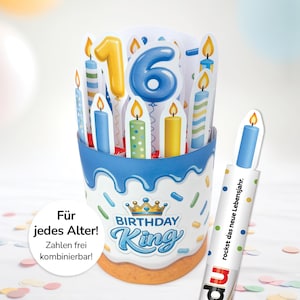 Peut inclure: Un présentoir en forme de gâteau d'anniversaire bleu et blanc, contenant des bougies colorées et le chiffre 16. Les mots "BIRTHDAY KING" sont imprimés sur le devant. Un élément séparé en forme de bougie est également visible.