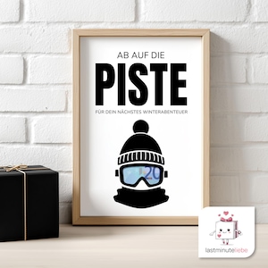 Puede incluir: Un cartel enmarcado con las palabras "AB AUF DIE PISTE" y "FÜR DEIN NÄCHSTES WINTERABENTEUER" en negro. La imagen presenta una ilustración en blanco y negro de un gorro de invierno, gafas y una bufanda. Una caja de regalo negra está a la izquierda.