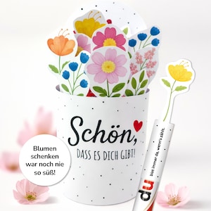 Könnte beinhalten: Ein weißer Behälter mit schwarzem Punktmuster und den Worten "Schön, DASS ES DICH GIBT!" in schwarzer Schrift, der bunte Papierblumen enthält. Rechts ist ein Stift mit einer gelben Blume. Der Text "Blumen schenken war noch nie so süß!" befindet sich in einem weißen Kreis.