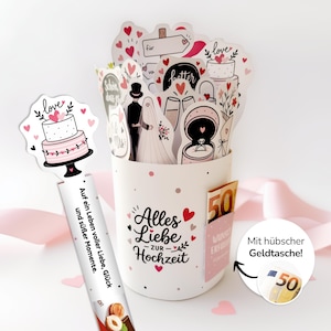 Pode incluir: Um recipiente de presente de cerâmica branca com decorações temáticas de casamento, incluindo adesivos em forma de coração e ilustrações de um bolo de casamento, um casal e um anel. O recipiente tem um bolso com uma nota de 50 euros e texto em alemão.