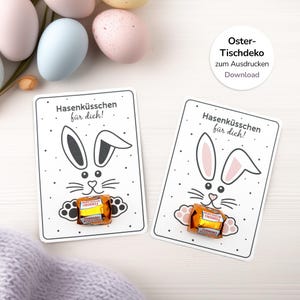 Könnte beinhalten: Zwei weiße Karten mit einem Hasengesichtsdesign, die ein verpacktes Schokoladenbonbon halten. Die Karten tragen den Text "Hasenküsschen für dich!" und sind mit kleinen schwarzen Punkten verziert. Osterthema.