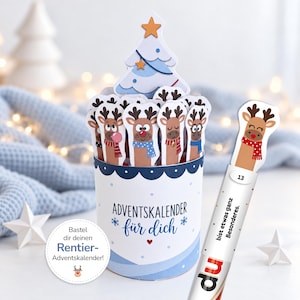 Könnte beinhalten: Ein zylindrischer Adventskalender mit blau-weißem Design und der Aufschrift "ADVENTSKALENDER für dich". Der Behälter enthält mehrere Rentier-Papieraufsteller und einen Weihnachtsbaum, wobei ein Rentier-Stab mit der Aufschrift "13" und "bist etwas ganz Besonderes" zu sehen ist.