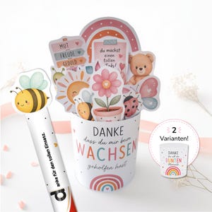 Könnte beinhalten: Ein weißer zylindrischer Behälter mit dem Text "DANKE dass du mir beim WACHSEN geholfen hast" und einem Regenbogen. Er ist gefüllt mit bunten Papieraufstellern wie einem Teddybären, einer Blume, einer Biene, einem Marienkäfer und einer Sonne.