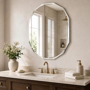 May include: A wall-mounted mirror with a faceted, multi-sided edge design. The mirror features a clear reflective surface with beveled edges, reflecting a bathroom interior with a window, a brass faucet, a vase with white flowers, and towels.