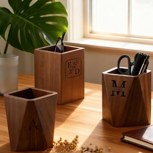 Può includere: Tre organizer da scrivania in legno con design geometrici. Uno contiene occhiali, un altro ha forbici e penne, e il terzo è vuoto. Ogni organizer ha un'iniziale o un monogramma personalizzato. Gli organizer sono in legno dai toni caldi.