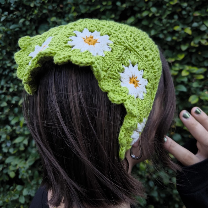 May include: A lime green crochet headband with white and yellow daisy appliqu&eacute;s. The headband has a scalloped edge and is worn on the head. The crochet work is visible and the daisies are evenly spaced.