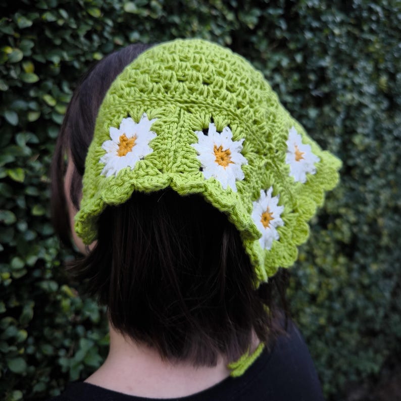May include: A lime green crochet bandana with white daisy appliqu&eacute;s. The bandana has a scalloped edge and is tied in the back. The daisies have yellow centers. The bandana is handmade.