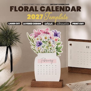 Könnte beinhalten: Ein 2027 Blumenkalender-Template in Glasform mit einem Februar-Kalenderblatt. Der obere Teil zeigt einen Blumenstrauß in Aquarelloptik mit rosa, weißen und violetten Blüten. Der Kalender steht auf einem rechteckigen Holzsockel.