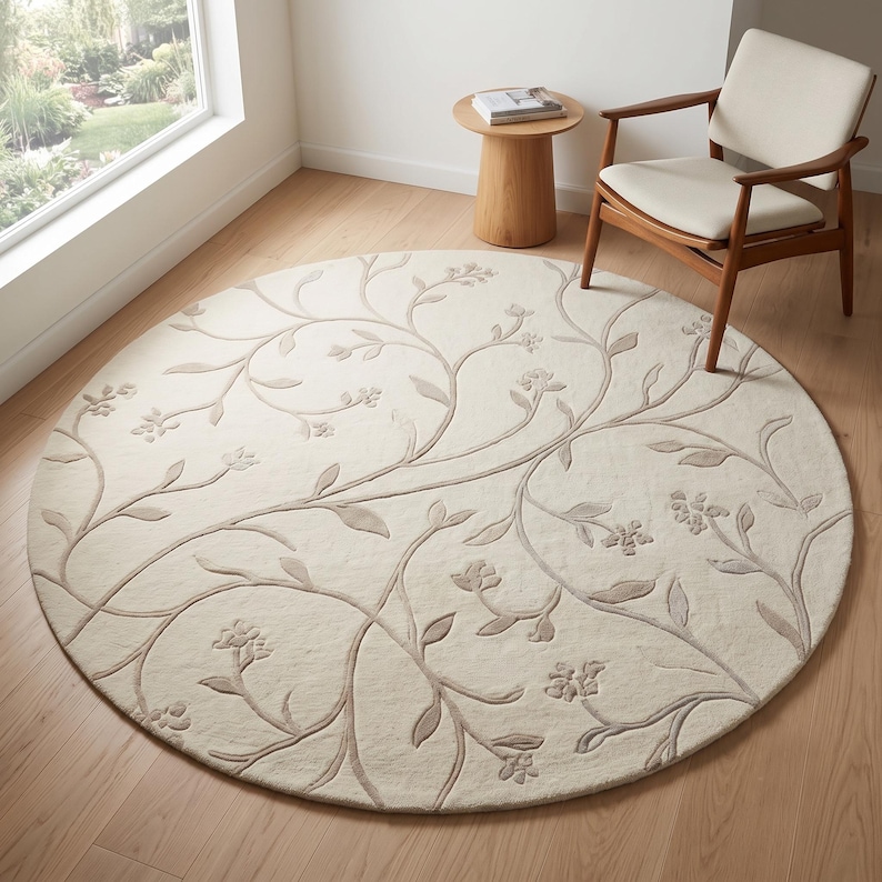 May include: A circular area rug featuring a cream-colored background with a raised, light beige botanical pattern of winding vines, leaves, and small flowers. The design is carved into the pile, creating a textured, tone-on-tone floral motif.