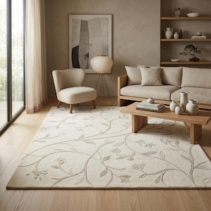 May include: A rectangular area rug featuring a cream-colored base with a raised, tone-on-tone botanical pattern of winding vines, leaves, and small flowers. The rug has a soft, textured surface and covers a portion of the light-colored wooden floor.