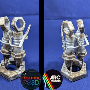 Può includere: Scultura stampata in 3D raffigurante due figure costruite con dadi, bulloni e altra ferramenta. Le figure sono collegate e poggiano su una base esagonale. La scultura ha un aspetto metallico usurato con toni marroni e grigi.