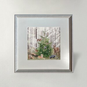 Op de afbeelding: Een ingelijste print met een versierde kerstboom in een besneeuwd bos, omringd door bosdieren zoals vossen, herten en een das. Het kunstwerk is gevat in een zilveren lijst.