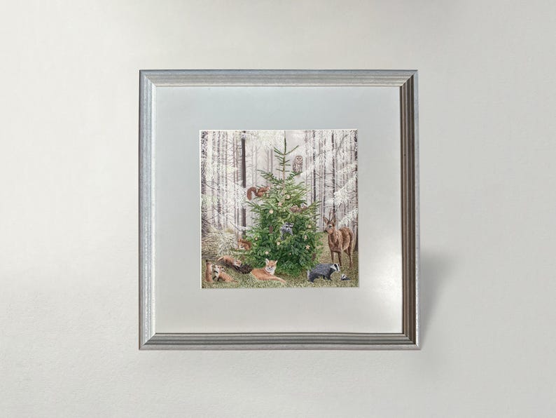 Op de afbeelding: Een ingelijste print met een versierde kerstboom in een besneeuwd bos, omringd door bosdieren zoals vossen, herten en een das. Het kunstwerk is gevat in een zilveren lijst.