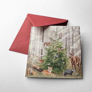 Op de afbeelding: Een kerstkaart met een boslandschap met een versierde kerstboom. Verschillende bosdieren, waaronder vossen, herten en een das, zijn rond de boom afgebeeld. Een rode envelop is zichtbaar op de achtergrond.
