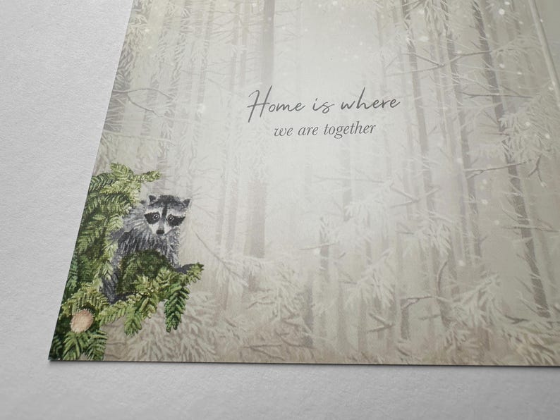 Op de afbeelding: Een wenskaart met een aquarel illustratie van een wasbeer op een dennentak. De achtergrond toont een mistige bossc&egrave;ne met de tekst "Home is where we are together".