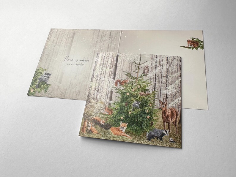 Op de afbeelding: Wenskaart met een winterse bossc&egrave;ne. De kaart toont een versierde kerstboom omringd door bosdieren, waaronder vossen, herten en eekhoorns. De tekst "Home is where we are together" staat aan de binnenkant.