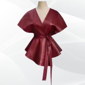 May include: A burgundy wrap top with a V-neck and short sleeves. The top has a belted waist and a flared peplum. The fabric has a slight sheen, and the garment is displayed on a mannequin against a white background.