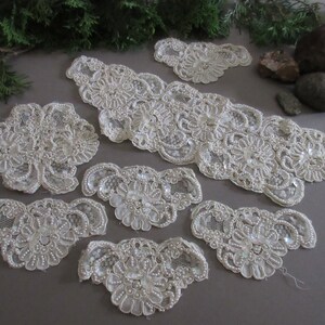May include: Ivory-colored lace appliques and trim, embellished with beads and sequins. The collection includes various shapes and sizes, including floral and scalloped designs. Perfect for embellishing garments or craft projects.