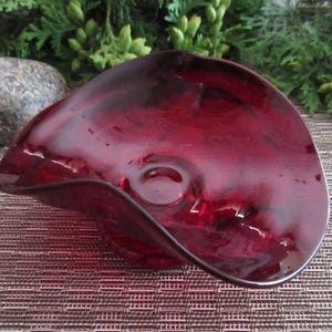 May include: A deep red glass dish with a wavy edge. The dish is made of glass and has a smooth, shiny finish.