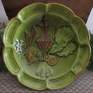 May include: A green ceramic serving dish with a raised design of vegetables and a pitcher. The dish has a scalloped edge and a textured surface.
