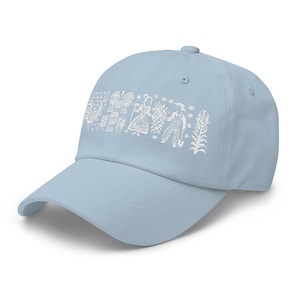 May include: A light blue baseball cap featuring a white graphic design of stylized figures and patterns across the front. The cap has a curved brim and an adjustable strap, offering a casual and comfortable fit. This hat is a stylish accessory for everyday wear.