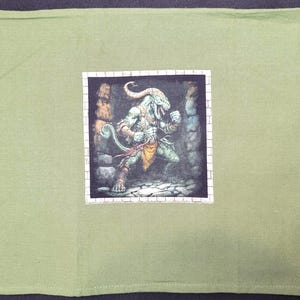 May include: A light green cloth with a square image of a fantasy creature. The creature is humanoid with reptilian features, wearing a loincloth and holding a weapon. The image is framed with a white brick-like border.