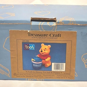 May include: A light blue box featuring a Treasure Craft label with a Winnie the Pooh salt and pepper set. The set includes a Pooh bear figurine and a honey pot. The box has illustrations of kitchen items.
