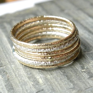 May include: A set of six thin gold and silver rings stacked together. The rings have a hammered texture.