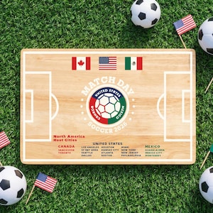 May include: A wooden soccer-themed display with the text "MATCH DAY SOCCER 2026" and flags of Canada, the United States, and Mexico. Soccer balls and miniature flags are scattered on a green grass background.