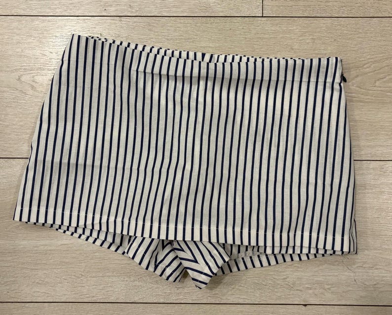 May include: White and navy blue striped shorts. The shorts have a high waist and a zipper closure. The fabric is a lightweight material, perfect for warm weather.