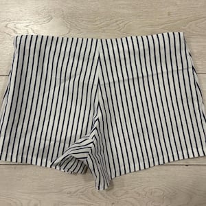 May include: White and navy blue striped shorts. The shorts have a high waist and a tailored fit. The vertical stripes create a slimming effect. The shorts are made of a lightweight fabric, perfect for warm weather.