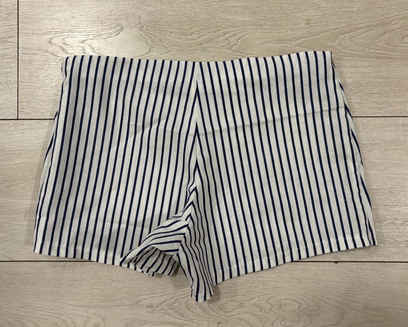 May include: White and navy blue striped shorts. The shorts have a high waist and a tailored fit. The vertical stripes create a slimming effect. The shorts are made of a lightweight fabric, perfect for warm weather.