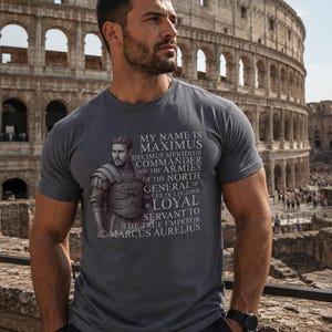 May include: A charcoal grey short-sleeved t-shirt featuring a graphic of a Roman soldier in armour and the text: MY NAME IS MAXIMUS DECIMUS MERIDIUS COMMANDER OF THE ARMIES OF THE NORTH GENERAL OF THE FELIX LEGIONS LOYAL SERVANT TO THE TRUE EMPEROR MARCUS AURELIUS.