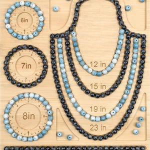 May include: A wooden bead design board featuring circular channels for bracelets labeled 6in, 7in, and 8in, and U-shaped channels for necklaces labeled 12in, 15in, 19in, and 23in. The board contains various light blue and black beads arranged in patterns.