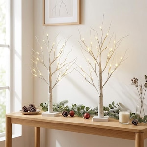 May include: Two artificial birch tree lamps with white textured trunks and thin, branching limbs. Each tree features small, warm white LED lights attached to the twigs and stands on a square white base. The trees are illuminated from within.
