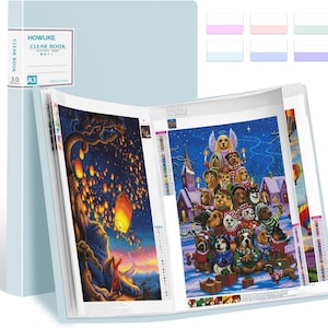 May include: A light blue A3 clear book with 30 pockets, displaying two diamond painting art pieces. One page shows a person under a tree with floating lanterns, and the other shows a group of dogs in winter attire. Includes six small color-coded labels.