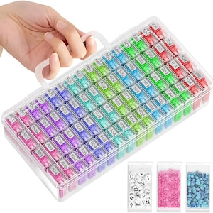 May include: Clear plastic organizer with a white handle, filled with small, colorful diamond painting drills. The organizer has multiple compartments labeled with numbers and letters. Three small bags of craft supplies are visible.