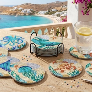 May include: A set of round drink coasters featuring colorful diamond art designs of sea creatures including an octopus, seahorse, whale, jellyfish, turtle, and starfish, accompanied by a black metal holder and a stylus tool for application.