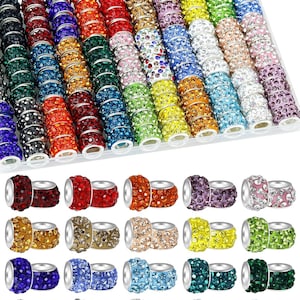 May include: A collection of cylindrical beads featuring embedded rhinestones in a wide variety of colors including red, blue, green, yellow, purple, orange, black, white, and multi-colored patterns, arranged in a clear plastic storage tray.