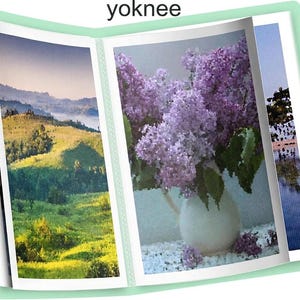 May include: A photo album with a light green cover, open to display three images. The center image features a still life of purple lilacs in a white vase. The other images show a landscape and a body of water.