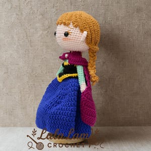 Puede incluir: Mu&ntilde;eca de ganchillo hecha a mano que se asemeja a un personaje de una popular pel&iacute;cula de animaci&oacute;n. La mu&ntilde;eca tiene un vestido azul, una capa morada y una trenza rubia. La mu&ntilde;eca mide unos 15 cm de altura.