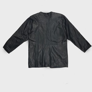 May include: A black leather jacket with a round neckline and long sleeves. The jacket is laid flat, showcasing its tailored design and seams. The leather appears slightly textured.