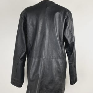 May include: A black leather coat displayed on a mannequin. The coat has a classic design with a collarless neckline, long sleeves, and a mid-thigh length. The leather appears smooth and has visible stitching details.
