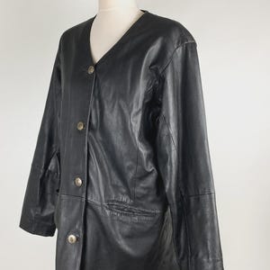 May include: Black leather jacket with a V-neckline and three silver-toned buttons. The jacket has two front pockets and is displayed on a mannequin. The jacket is a classic style.