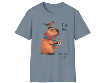 May include: A blue t-shirt featuring a cartoon capybara wearing a colorful scarf and holding a coffee cup. A small bird sits on the capybara's head. The text "I'M FINE" and "EVERYTHING IS FINE" are printed on the shirt.