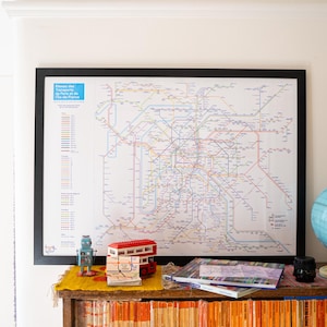 Può includere: Una mappa incorniciata del sistema di trasporto pubblico di una città è appesa sopra una mensola con un mappamondo, libri e oggetti decorativi. La mappa è dettagliata con linee colorate. Un piccolo robot giocattolo e un modello di autobus a due piani rosso sono sulla mensola.
