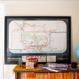 Könnte beinhalten: Eine gerahmte Karte des öffentlichen Verkehrssystems einer Stadt hängt an einer Wand. Ein Globus, ein Spielzeugbus und andere dekorative Gegenstände stehen auf einem Holzregal unter der Karte. Der Globus ist hellblau und gelb.