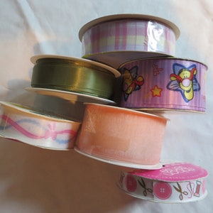 May include: Assortment of six spools of ribbon in various colors and patterns, including pink, green, peach, and white with a cartoon character design.